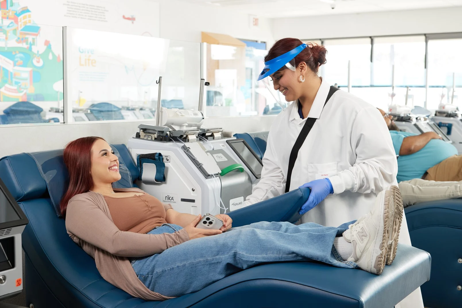 Woman donating plasma and a female phlebotomist in a white lab coat