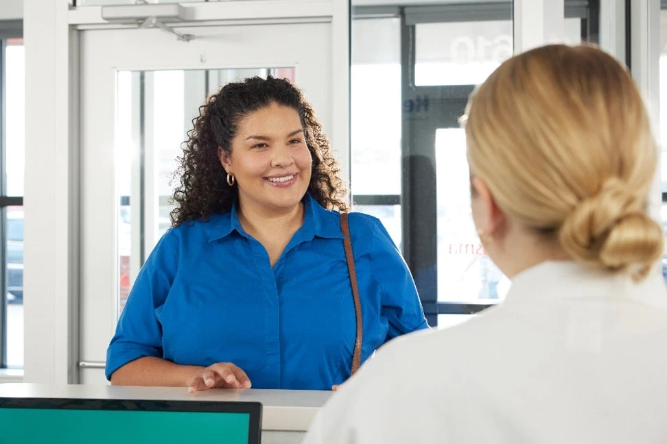 A woman speaking to a reception tech in a white lab coat